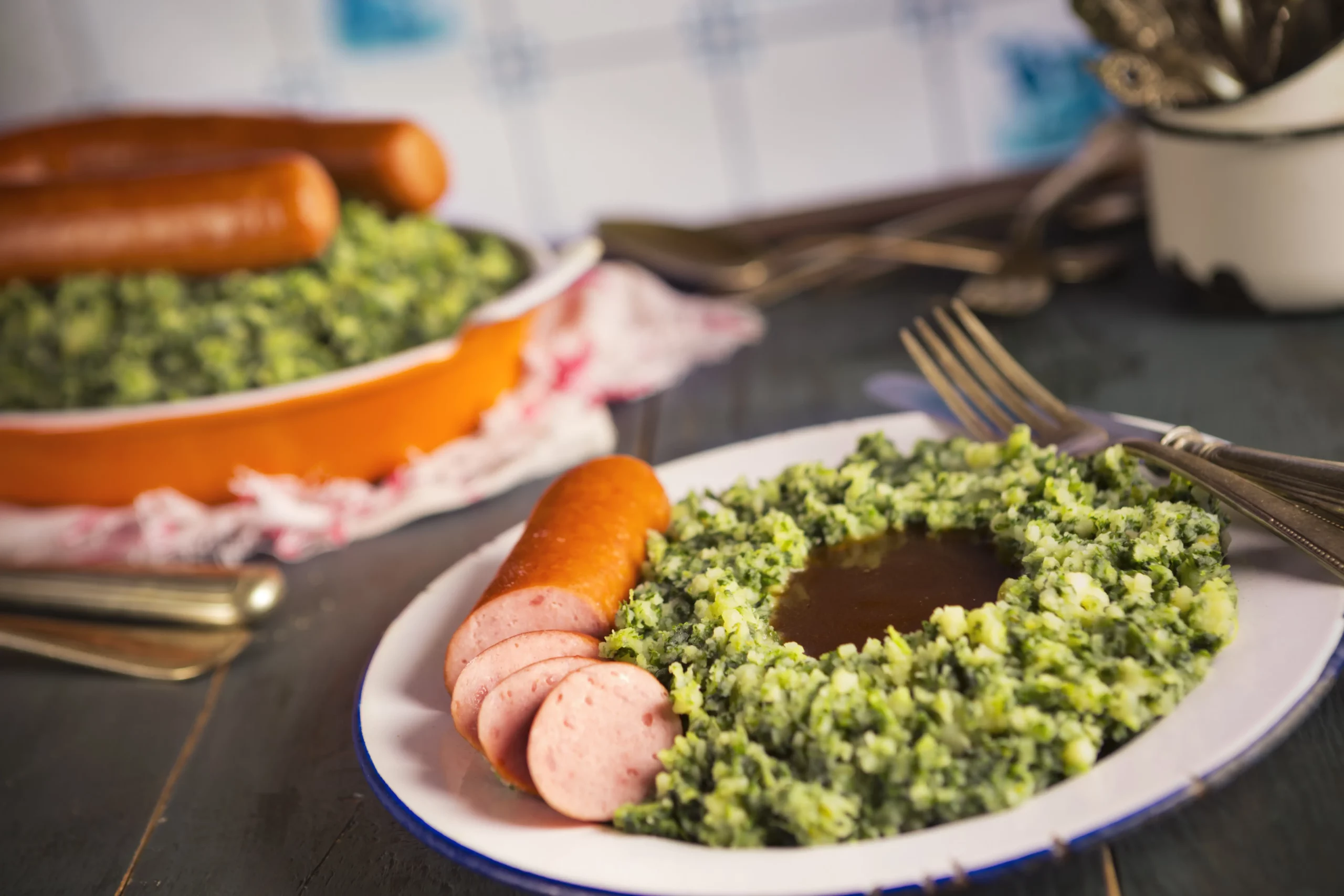 A plate with 'Boerenkool Stamppot' or mashed potato with kale and smoked sausage, a traditional Dutch meal.